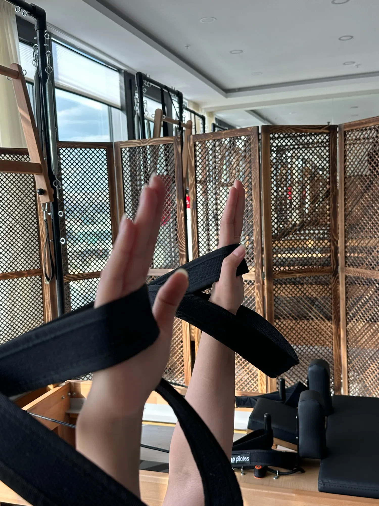 Reformer kayışlarını tutan eller; arkada ahşap kafesli paravan ve stüdyonun tavanı.